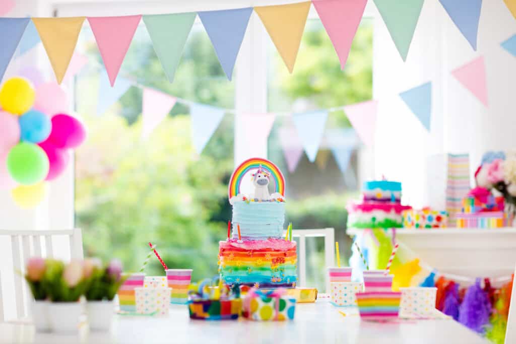 Kids birthday party decoration and cake. Decorated table for child birthday celebration. Rainbow unicorn cake for little girl. Room with festive balloons, colorful banners 